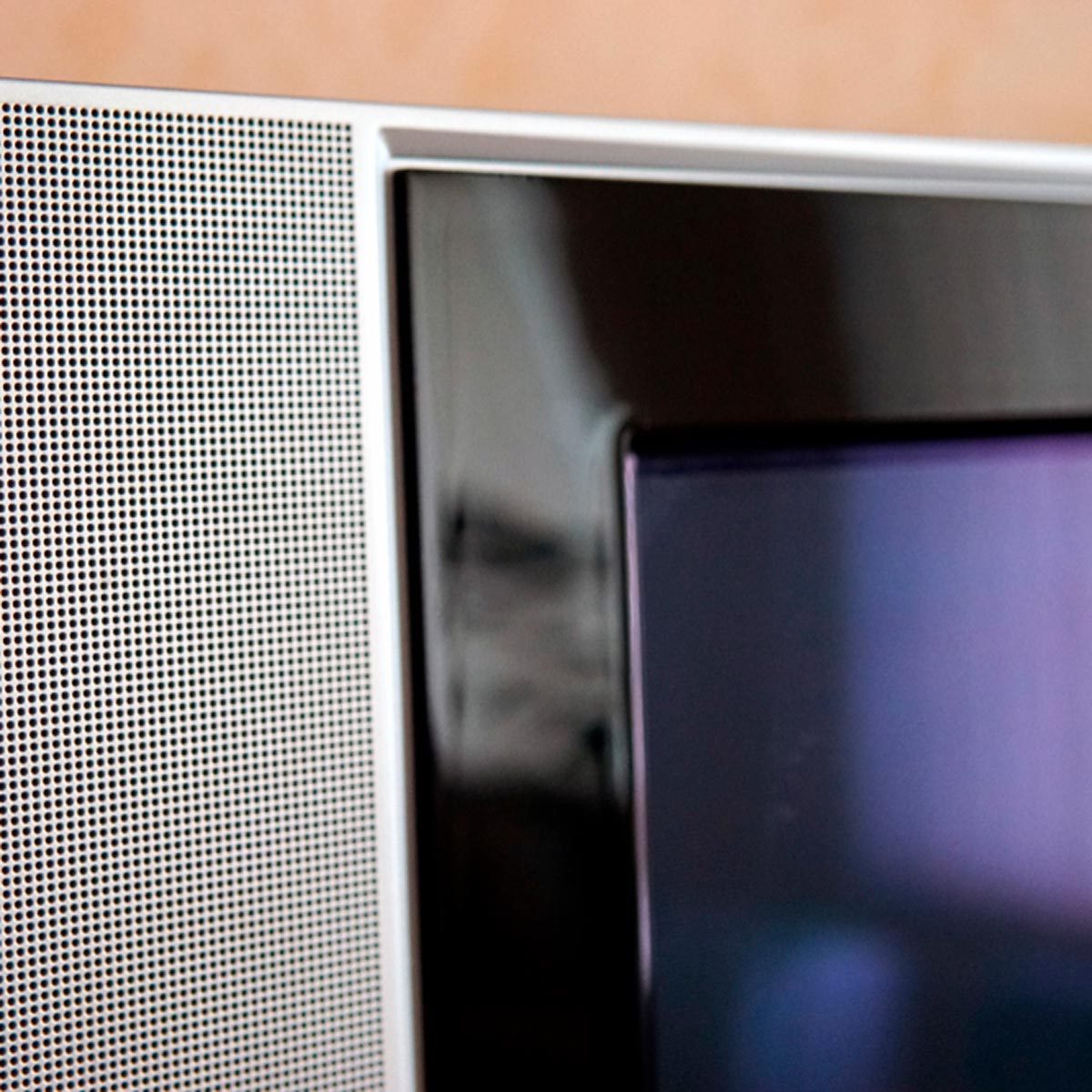 A close-up of a television's edge, featuring a sleek black screen and a textured metallic speaker grill, suggesting modern technology in a minimalistic setting.