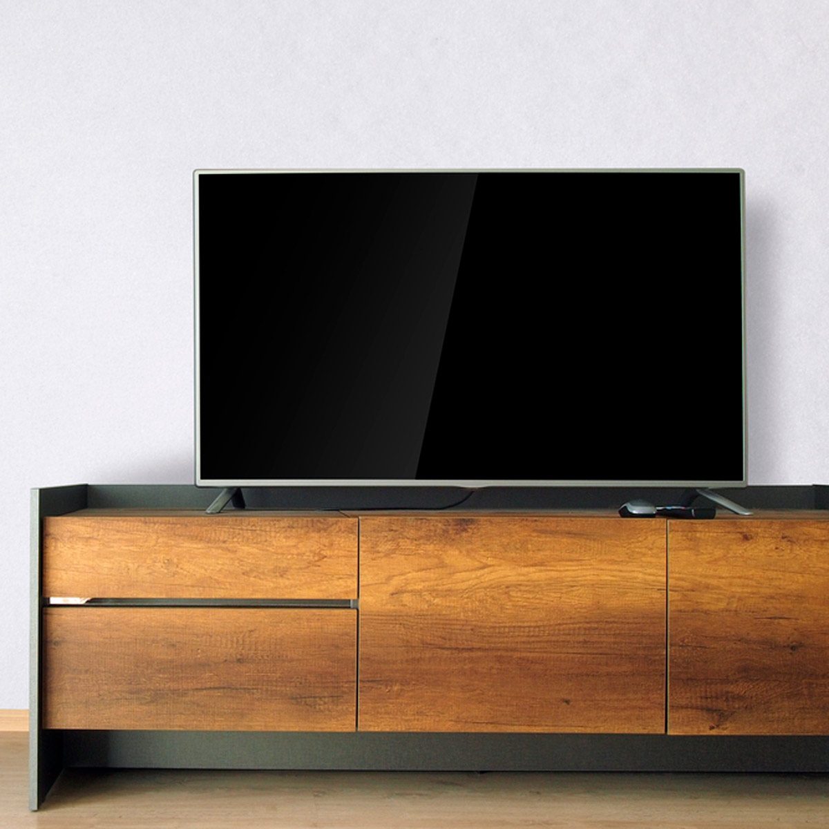A modern television rests on a wooden cabinet, displaying a blank screen in a minimalist room with a light-colored wall.