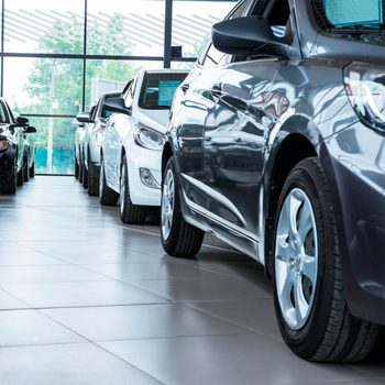 Multiple cars are parked in a showroom, showcasing their polished surfaces under natural light filtering through large windows.