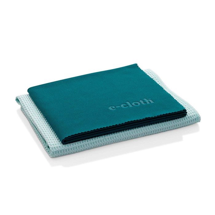 Two cleaning cloths are neatly stacked, one teal and one light blue, resting on a flat surface. The teal cloth has 