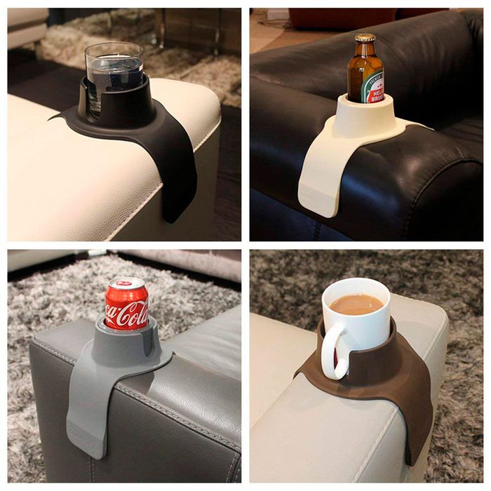 Four cup holders, each cradling a different beverage, are placed on sofa armrests in a cozy living room setting with a soft rug.
