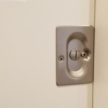 A metal door lock is mounted on a white door. The lock's knob is turned, indicating it is in the locked position.