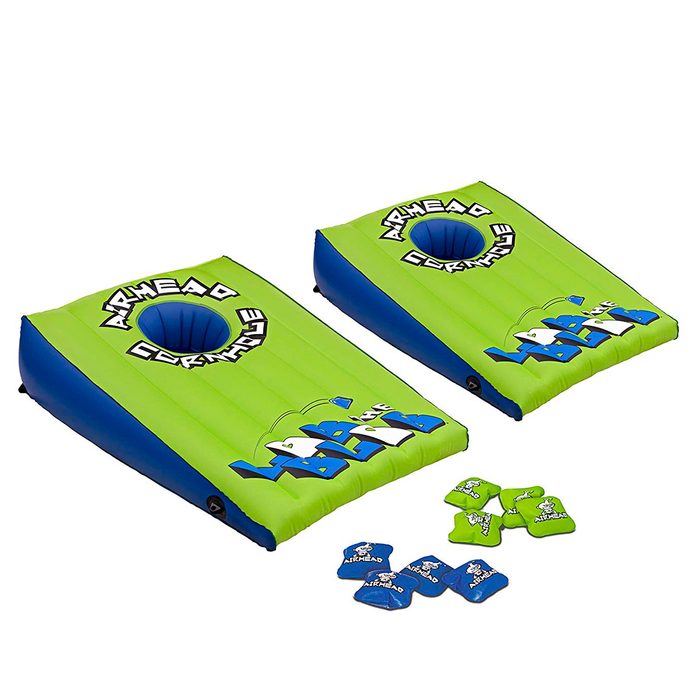 Two inflatable cornhole boards sit side by side, brightly colored in green and blue, with several cornhole bean bags scattered nearby.
