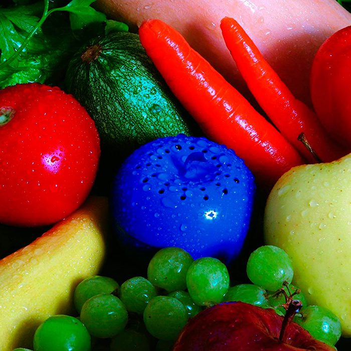A blue object sits among vibrant, wet fruits and vegetables, including apples, grapes, carrots, and zucchini, in a colorful, fresh arrangement.