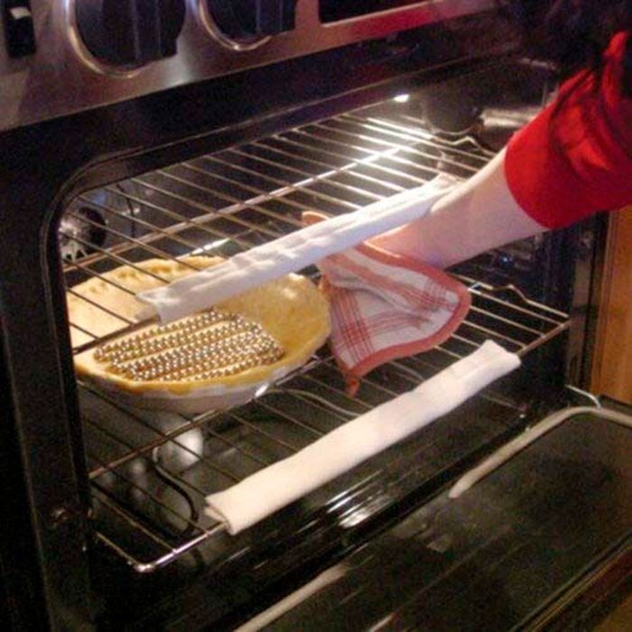 A hand removes a pie from the oven, using a towel for protection, while a partially baked pie rests on the rack inside the oven.