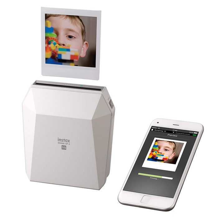 A photo printer prints a colorful image of a boy manipulating toys, with a smartphone displaying a preview of the image and a progress bar below.