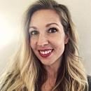 A woman with long, wavy blonde hair smiles. She is positioned against a neutral-colored background, exhibiting warmth and approachability in her expression.