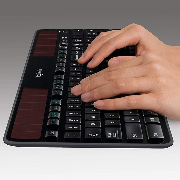 A black keyboard is being used, fingers are typing on the keys, with a gradient gray background showcasing its sleek design.