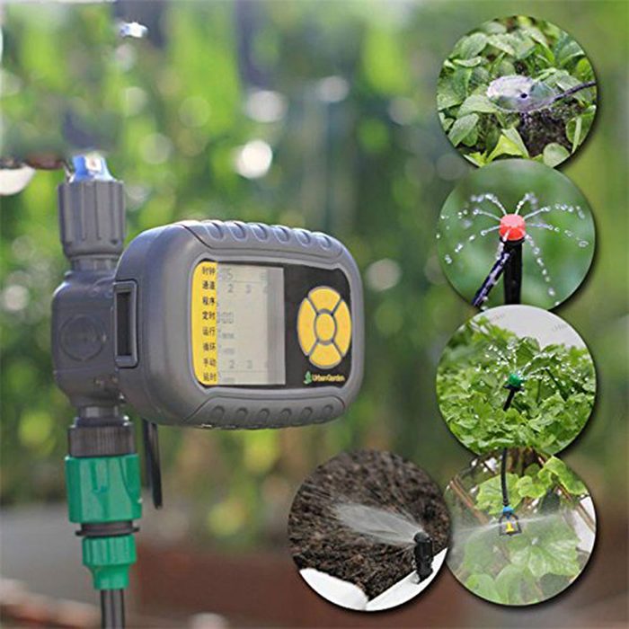 A digital irrigation timer displays settings while connected to a water source. Nearby, various plants are watered through multiple sprinkler systems in a garden setting.