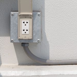 An electrical outlet is mounted on a wall, featuring multiple sockets. A gray conduit is attached, providing connection to the building's electrical system.