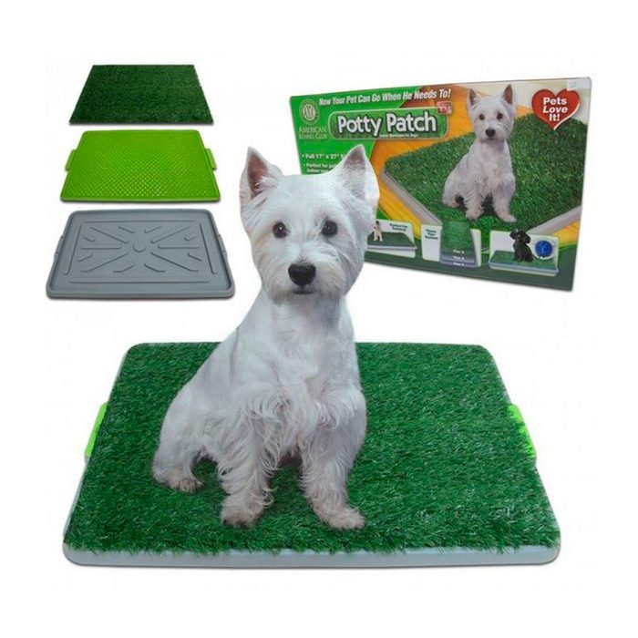 A small white dog sits on a green artificial grass potty patch, surrounded by additional components and packaging that promote its use for pet relief indoors.
