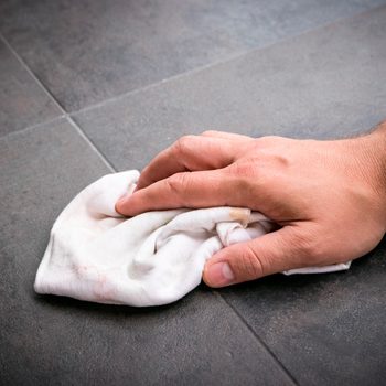 A hand wipes a cloth across a dark, textured floor surface, removing dirt or stains in a domestic or maintenance context.