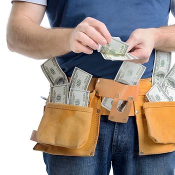 A person places money into a tool belt's pockets, with bills visibly spilling out, set against a plain white background.