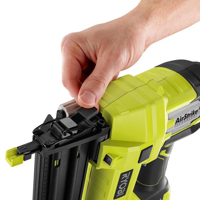 A hand is adjusting a component on a bright green and black air-powered nail gun, preparing it for use in a workspace setting.