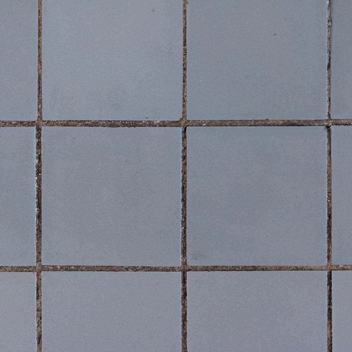 Gray ceramic tiles are arranged in a grid pattern, creating a uniform surface with visible grout lines, suggesting a clean, minimalist environment.