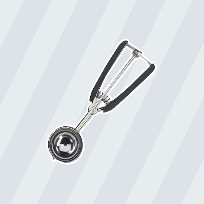 A metal ice cream scoop with a black handle is positioned centrally, ready for use against a light striped background.