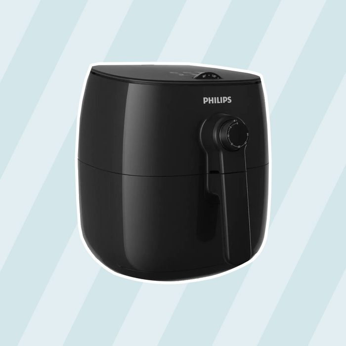 A black air fryer sits on a light blue striped background, showcasing its smooth exterior and a control knob on the front for cooking settings.