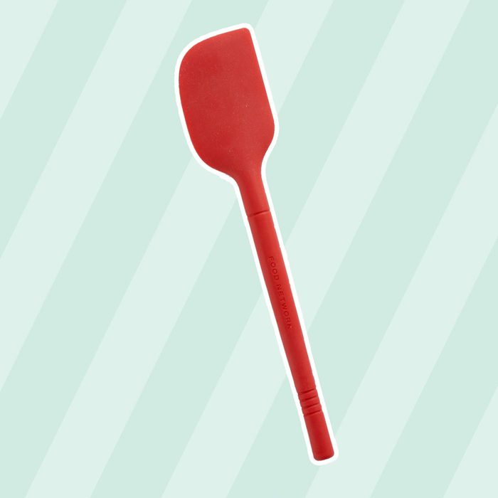 A red silicone spatula rests against a light green striped background, designed for mixing or flipping food in cooking.