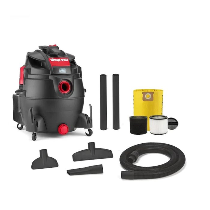 A black shop vacuum rests on wheels, surrounded by various attachments and filters, ready for cleaning tasks in a workshop or garage environment.