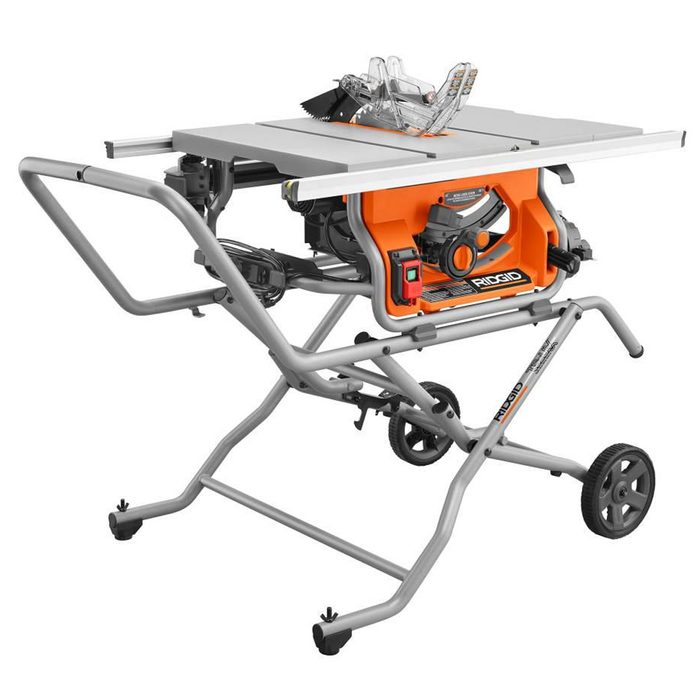 A table saw is positioned on a wheeled stand, ready for cutting wood, with a blade guard visible, surrounded by an open workspace.