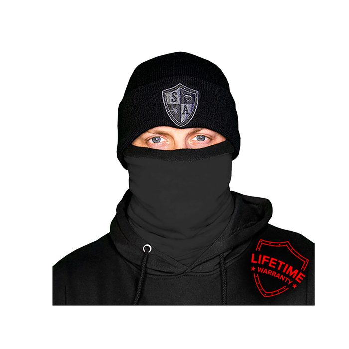 A person wears a black beanie and face covering, revealing only their eyes, while dressed in a black hoodie featuring a red 