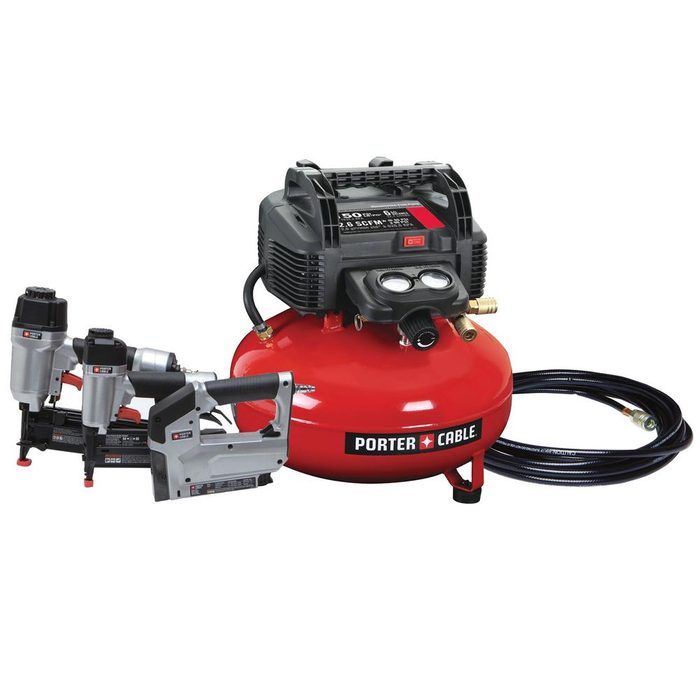 A red air compressor sits on a surface, connected to two nailers and a hose, ready for use in construction or home improvement tasks.