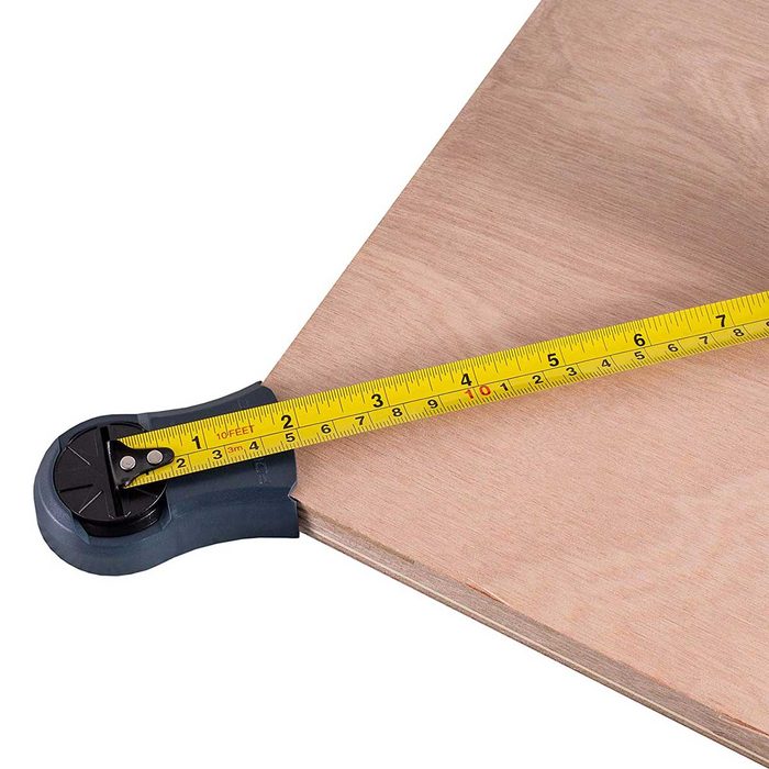 A tape measure is extended across a wooden surface, indicating measurements while resting on the edge, highlighting its utility in woodworking or construction tasks.