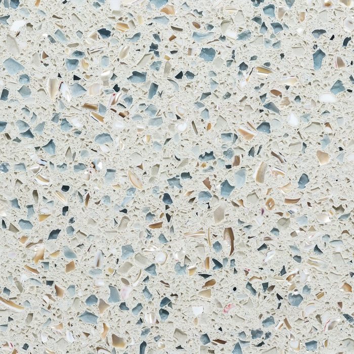 A textured surface features a blend of cream and light blue fragments, interspersed with shimmering pieces, creating a visually appealing, abstract pattern.