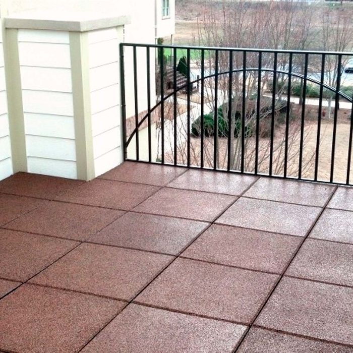A brown tiled balcony features a black railing. It overlooks a landscaped area with trees and pathways in a residential environment.