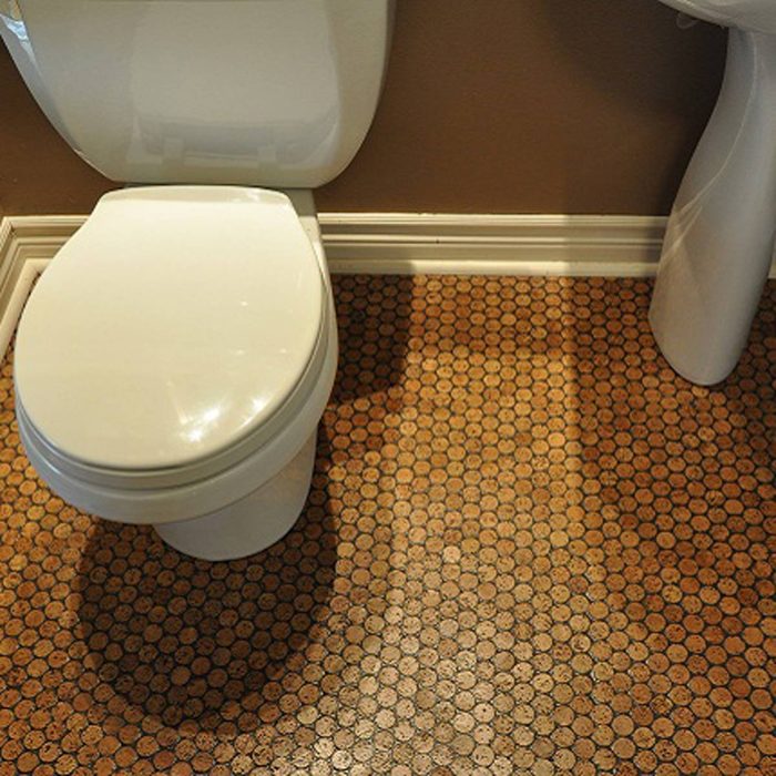 A white toilet sits beside a white pedestal sink, on a floor covered with circular brown tiles, in a warmly painted bathroom.