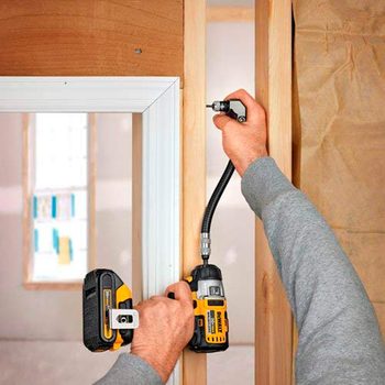 A person uses a cordless drill to fasten a component to wooden framing inside a partially completed room. Natural light comes from a nearby window.