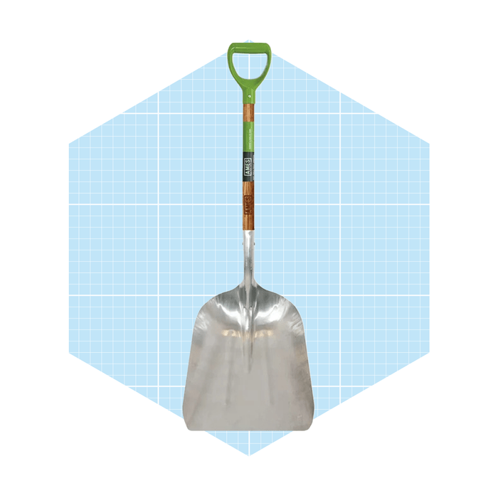 A metal shovel stands upright with a green handle, set against a light blue grid background, indicating a gardening or landscaping context.