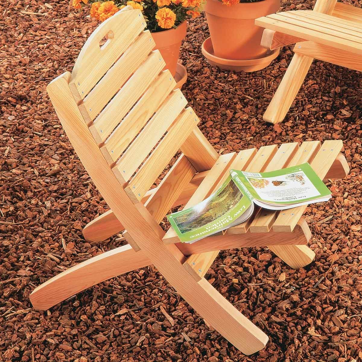 A wooden chair rests on a bed of mulch, holding an open book, surrounded by potted plants with orange flowers.
