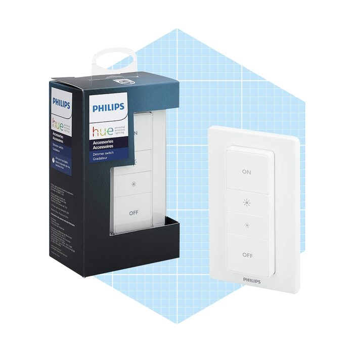 A Philips Hue dimmer switch is displayed next to its packaging, designed for controlling smart lighting. The background features a light blue grid pattern.