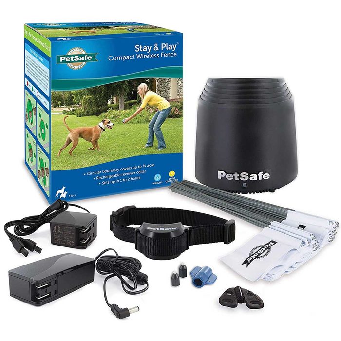 A wireless dog fence kit is displayed, featuring a boundary transmitter, receiver collar, installation tools, and instructional materials, set against a grassy outdoor area.