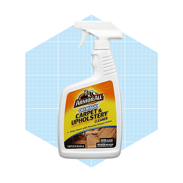 A spray bottle of Armor All Carpet & Upholstery Cleaner sits against a light blue grid background, ready for cleaning tasks related to carpets and upholstery.