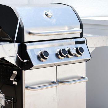 A stainless steel gas grill sits on a countertop, featuring four control knobs and a silver lid, showcasing a clean, modern outdoor cooking area.