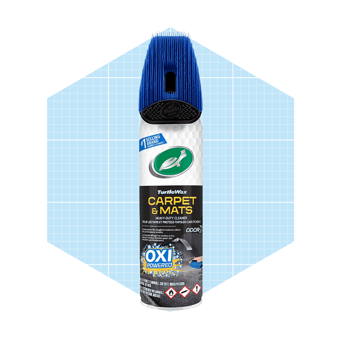 A spray can of TurtleWax Carpet & Mats cleaner sits against a light blue geometric background, designed for deep cleaning carpets and mats.