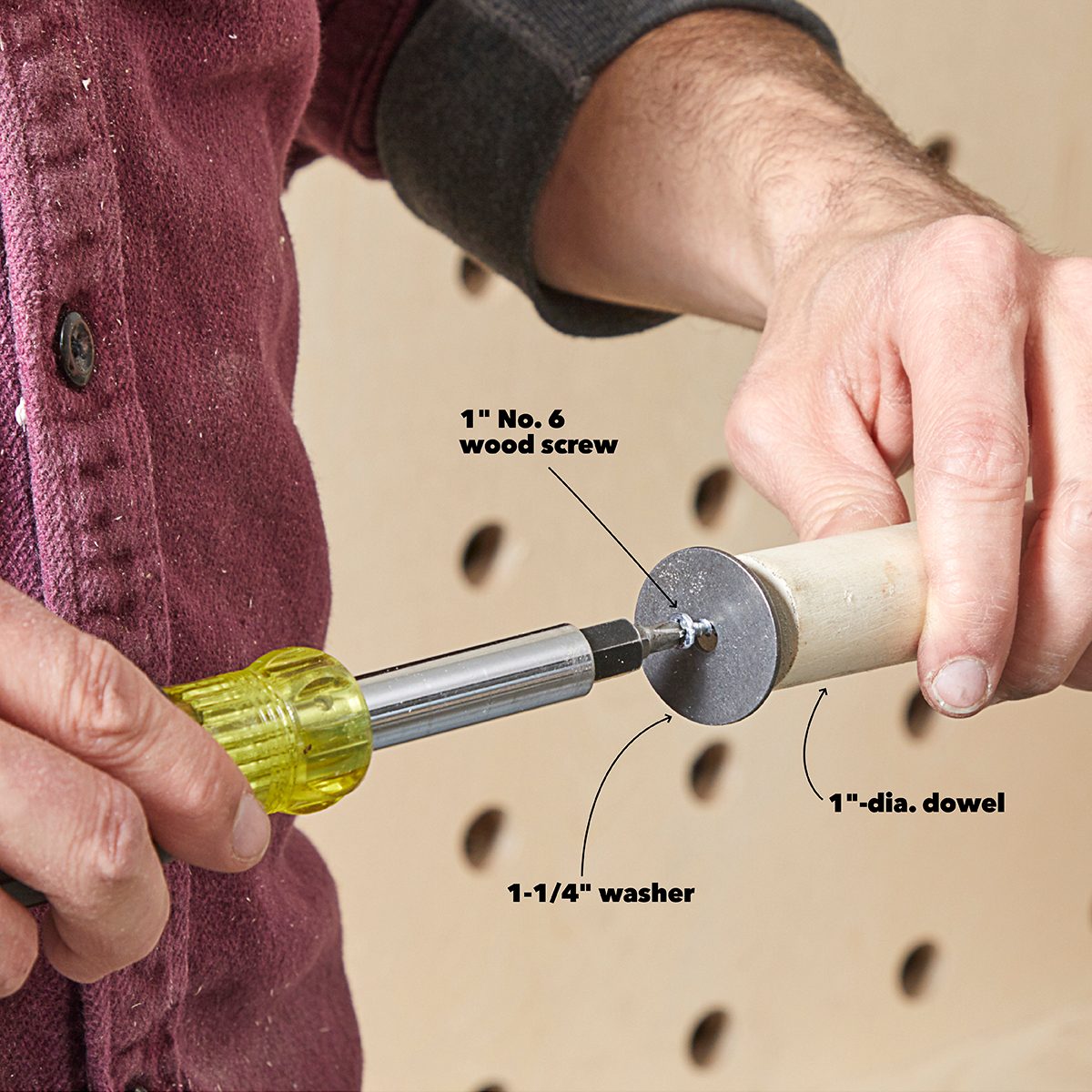 A person is using a screwdriver to insert a wood screw through a washer into a dowel, against a perforated background.