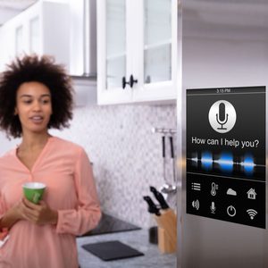 A woman stands in a kitchen, holding a green cup. A smart screen displays the message, 