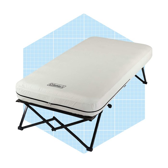 A rectangular cot mattress lies flat on a folding frame, designed for temporary sleeping arrangements, set against a light blue grid-patterned background.