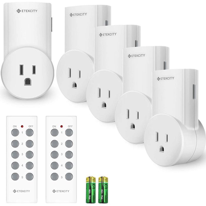 A set of white electrical plugs and remote controls is arranged neatly, with batteries placed below for powering the remotes, suggesting easy home automation.