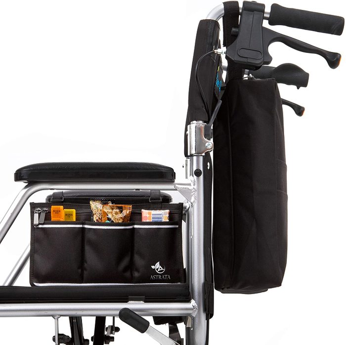 A wheelchair with a black seat has storage compartments containing snacks. It features an upright handle and support for mobility, set against a blank background.
