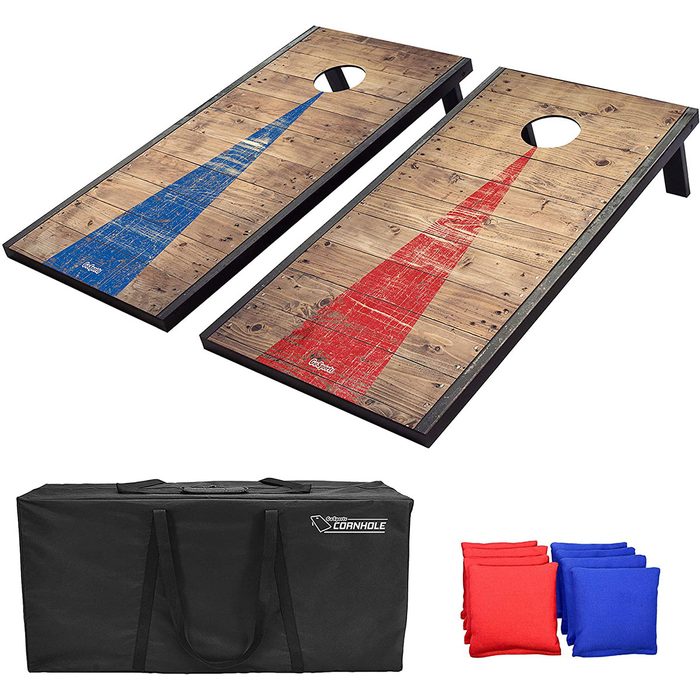Two cornhole boards, one with a blue design and the other in red, are positioned next to a black carrying bag and colored bean bags.