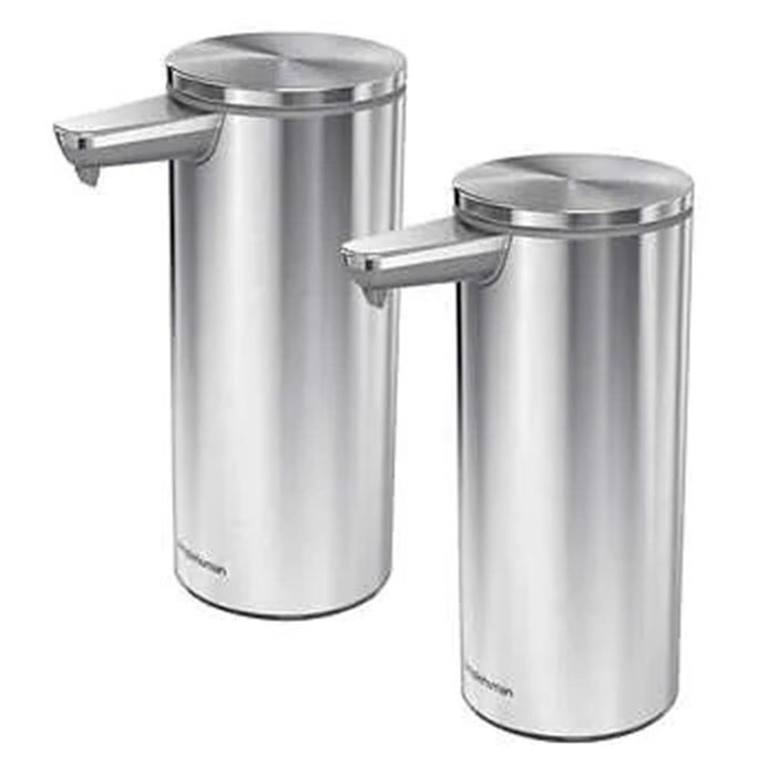 Two cylindrical stainless steel dispensers stand side by side, featuring push levers for dispensing liquid, possibly soap, in a clean, modern kitchen setting.