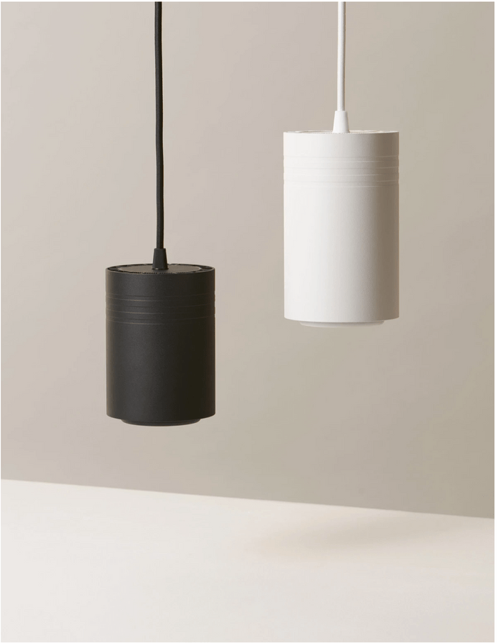 Two cylindrical pendant lights, one black and one white, hang from a ceiling on separate cords, against a soft, neutral background.