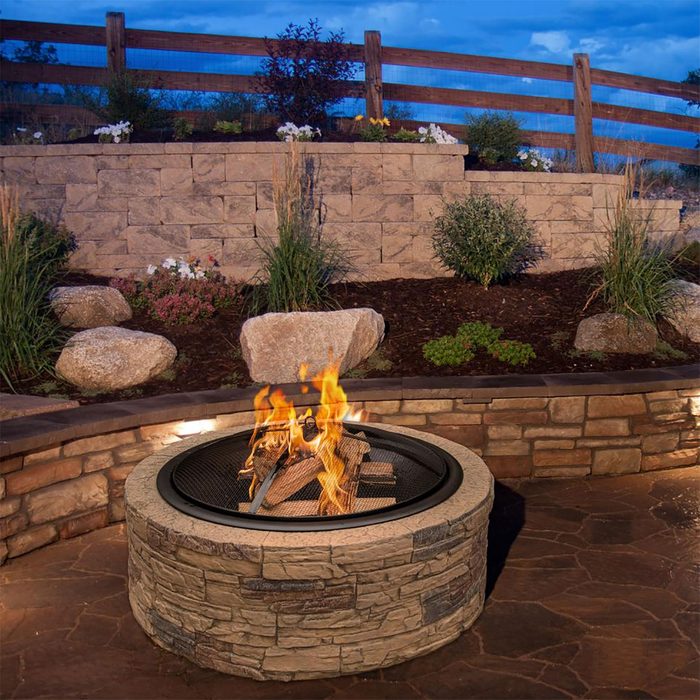 A stone fire pit burns logs, creating flames. It
