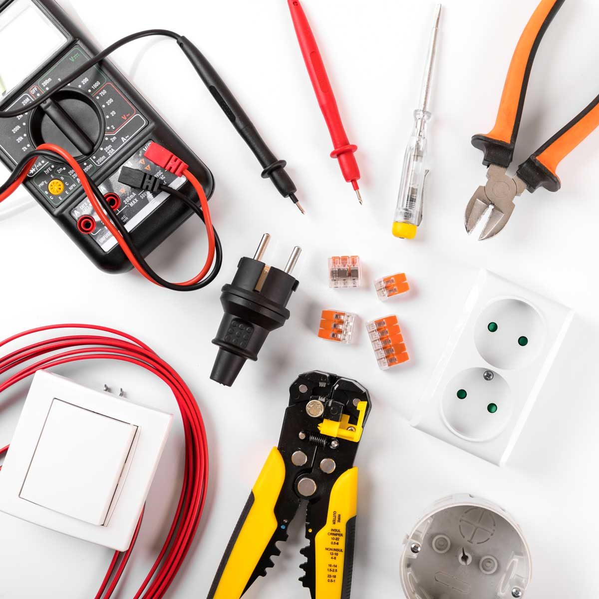 A variety of electrical tools and components are arranged on a white surface, including a multimeter, wires, connectors, a switch, and pliers.