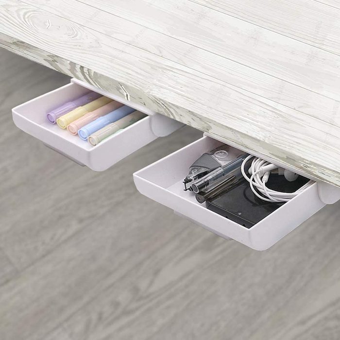 Two storage drawers, one with colored pens and the other with office supplies, are attached beneath a light-colored desk on a wooden floor.