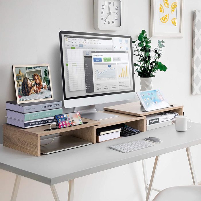 A sleek desk displays a computer, books, a photo frame, and plants, creating a modern workspace filled with organized technology and personal touches.